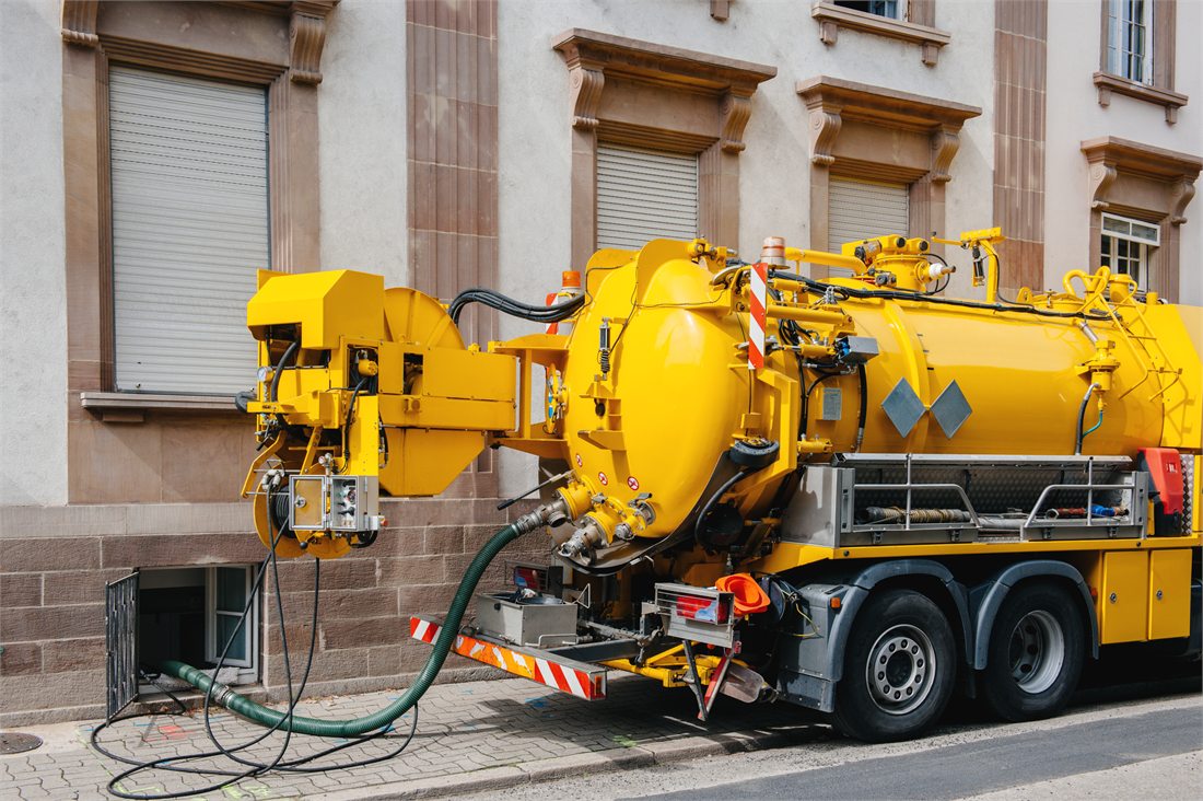 A yellow sewer service truck parked beside a building.