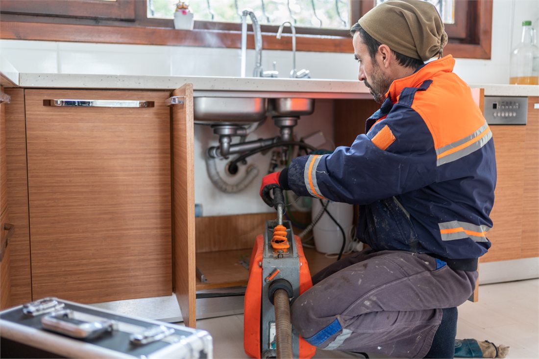 A technician clearing a drain under a sink with a machine.