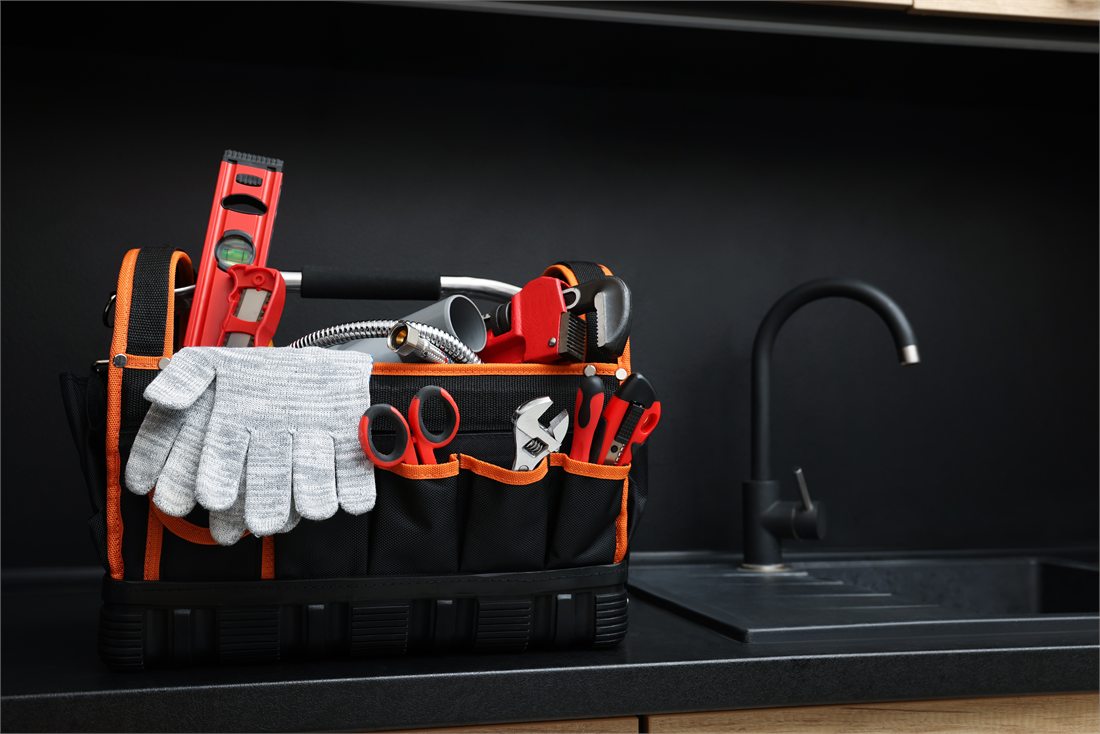 A tool bag with plumbing tools beside a dark sink.