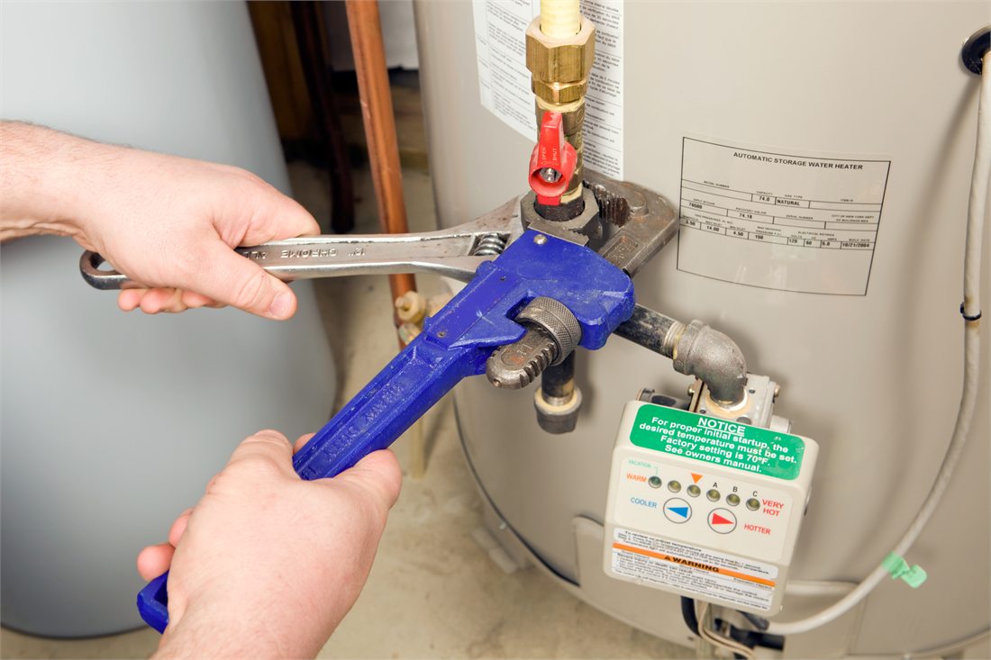 Hands tightening a fitting beside a water heater control panel.